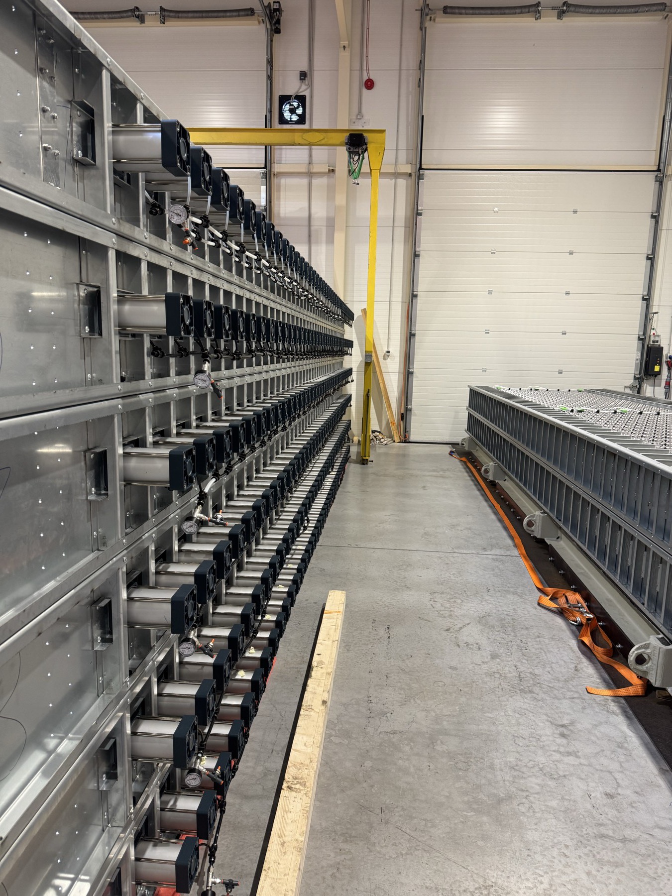 Compartment structures on the assembly floor, one lined with rows of inter-cell heat exchangers and pneumatic compression cylinders, the other holding installed cells.