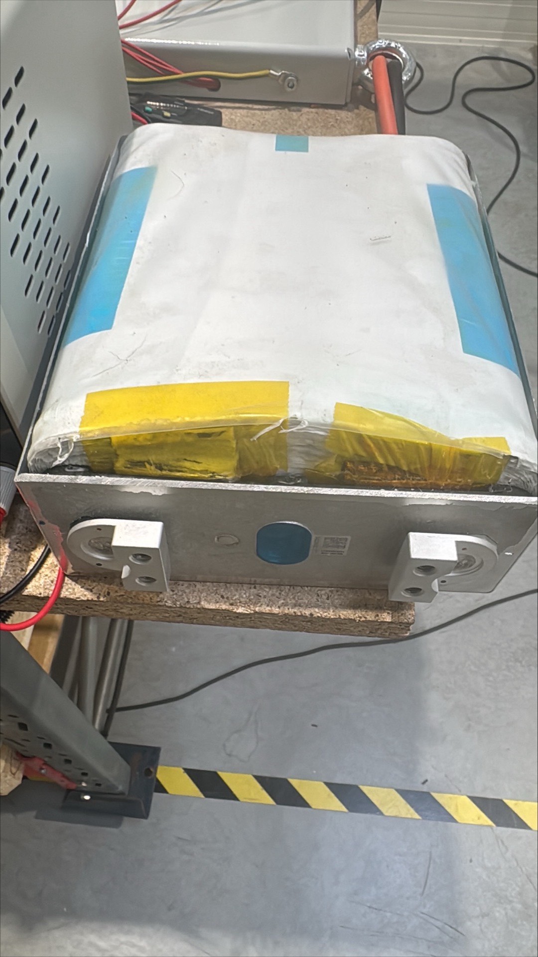 A prismatic cell with the can removed. The wound electrode stack, wrapped in film and tape, sits above the metal plate carrying the terminals.